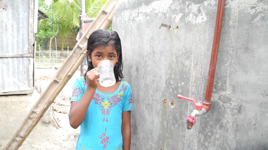 A girl enjoys a drink of water from a solar based purification system supplied by CAFOD, Bangladesh.