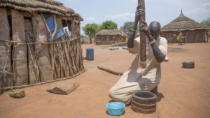 Mary kneels on the ground, using a pestle and mortar to make flour.