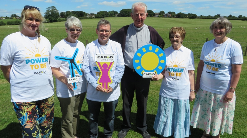 A group of CAFOD volunteers, including a priest, waaring tshirts and holding signs which support CAFOD's Power to be campaign