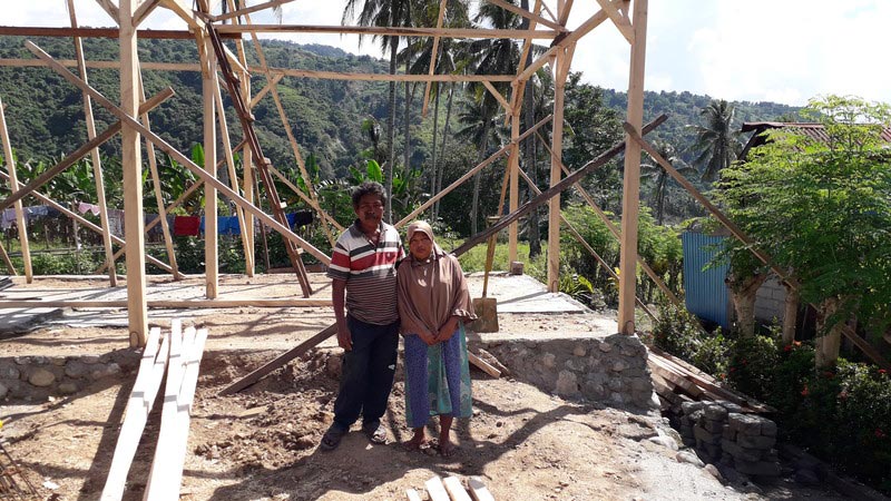 A family from Salua village stand in front of their new home