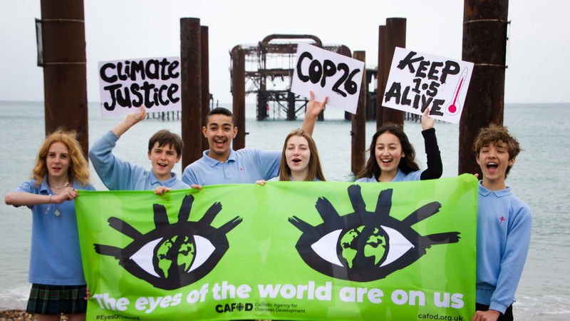 Six young campaigners hold a large banner showing two eye, which says: 'The eyes of the world are on us.'