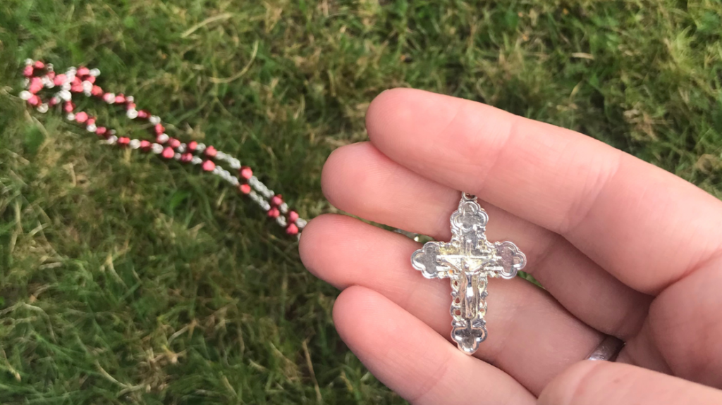 Hand holding rosary beads against grass.