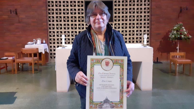 Sue Cooper, standing in front of an altar, holding her papal blessing