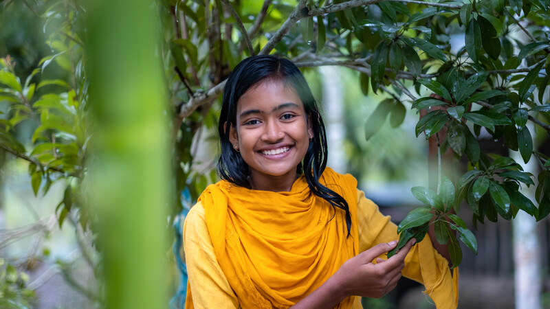 Smiling girl dressed in yellow next to a tree.