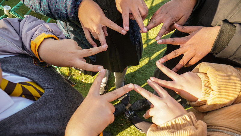 A group of children stand in a circle with their fingers touching in the centre of the image, making a star shape