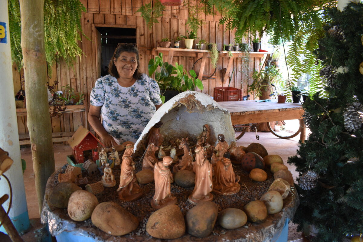 A woman stands behind a nativity set which is surrounded by rocks and made up of figures of Mary, baby Jesus, Joseph, Shepherds, Magi and various animals.